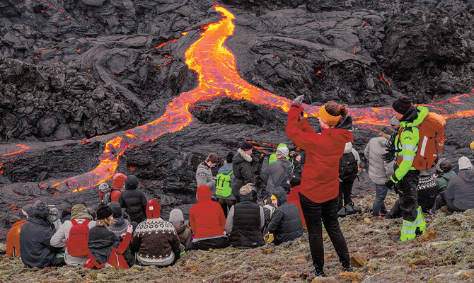 People taking pictures of lava coming from an active volcano