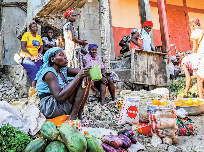 People gathered outside a crumbling building while making food with rice and fruit