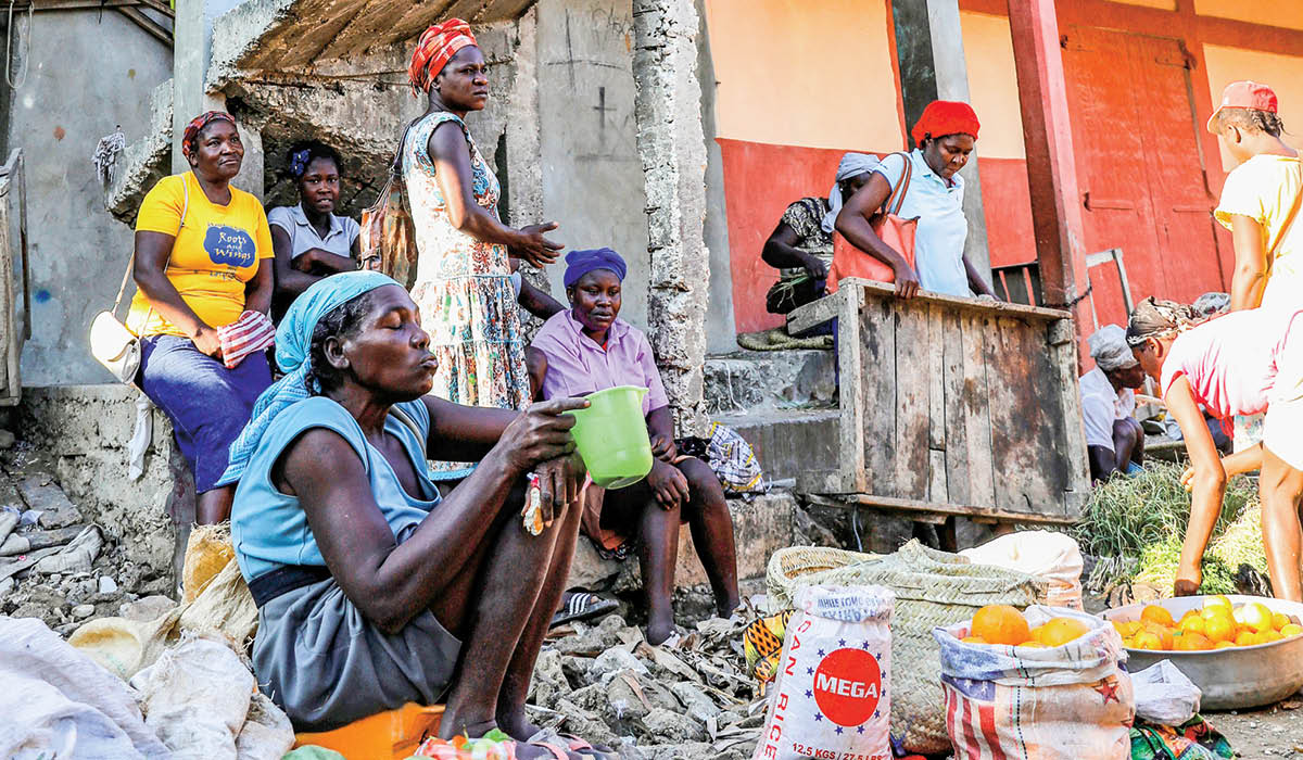 People gathered outside a crumbling building while making food with rice and fruit