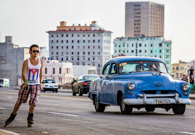 Photo of a person rollerblading in a city street next to an old-time car