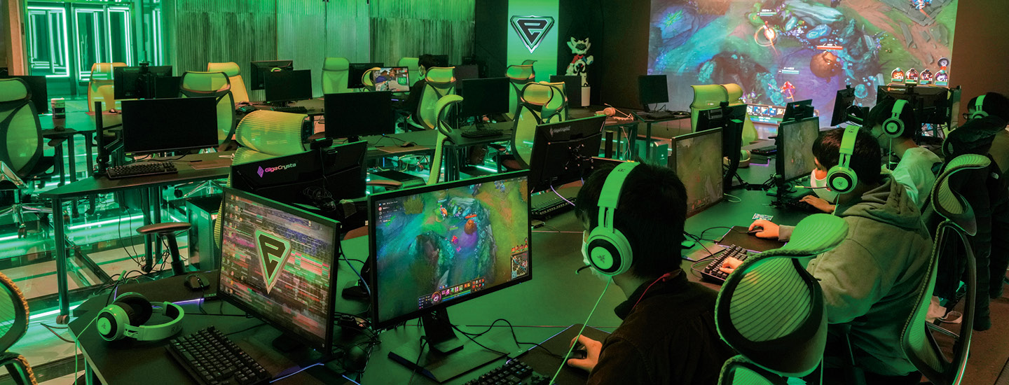 Photo of people all wearing headphones and playing videogames in a room on separate monitors